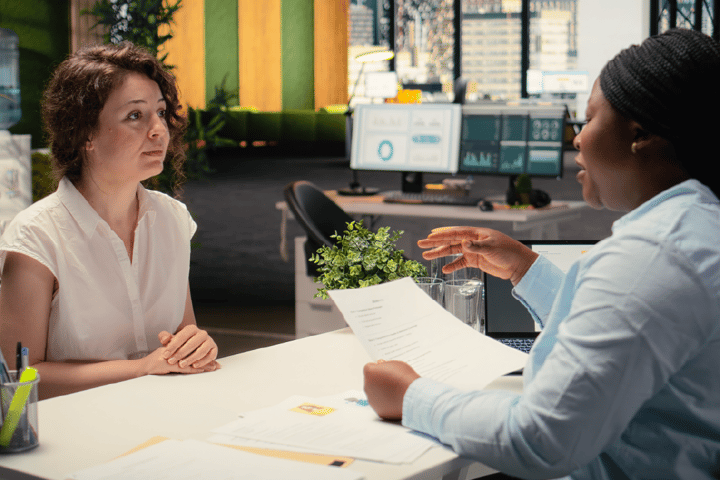 A doctor who is a black-skinned female is assessing another white-skinned woman with short brunette hair